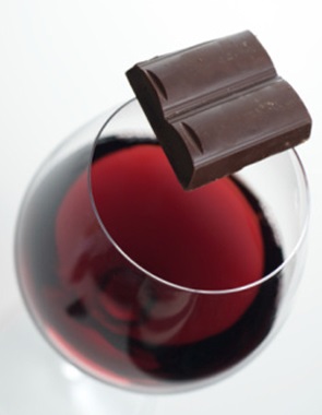 Piece of dark chocolate balanced on the rim of a glass of red wine