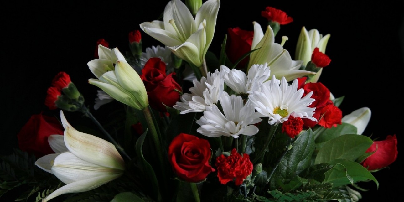 A sympathy arrangement of white lillies, red roses, and white daisies