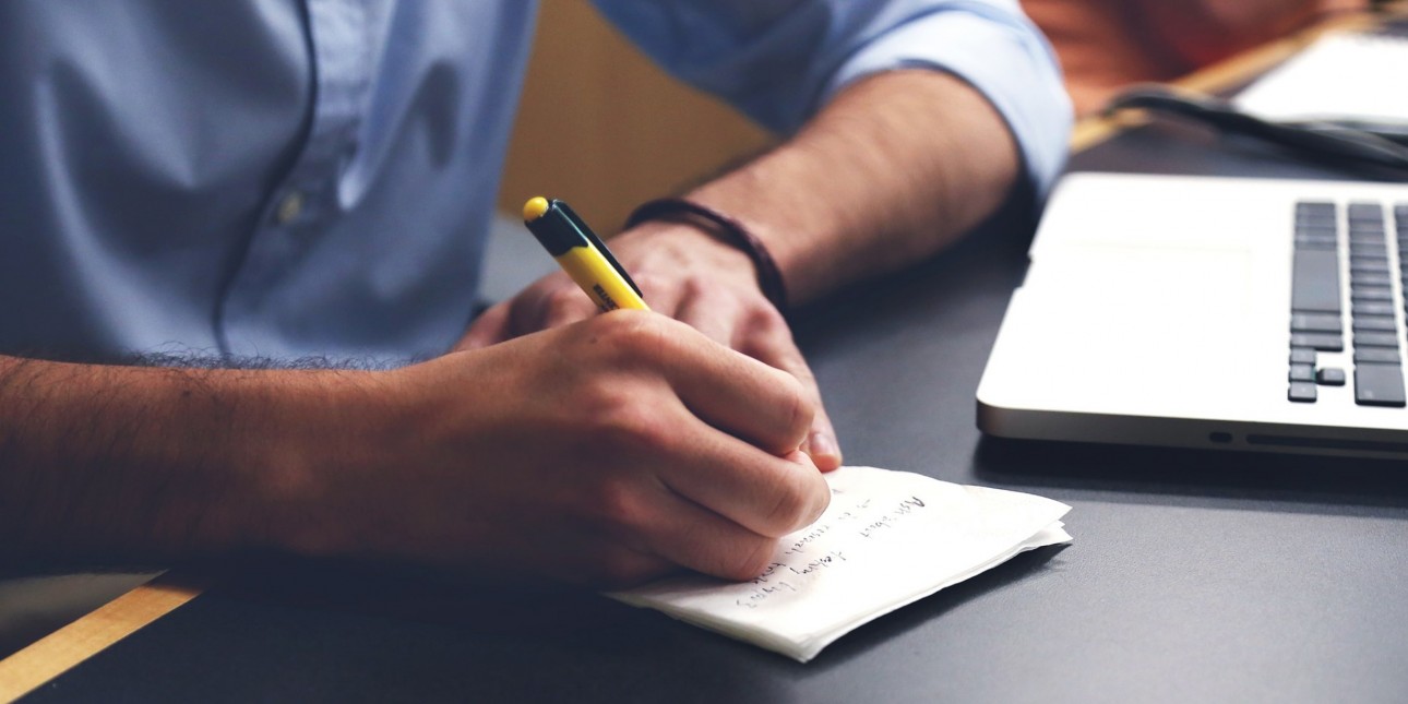 Person writing in front of a laptop