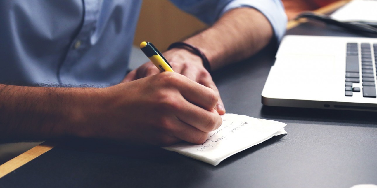 Person writing in front of a laptop