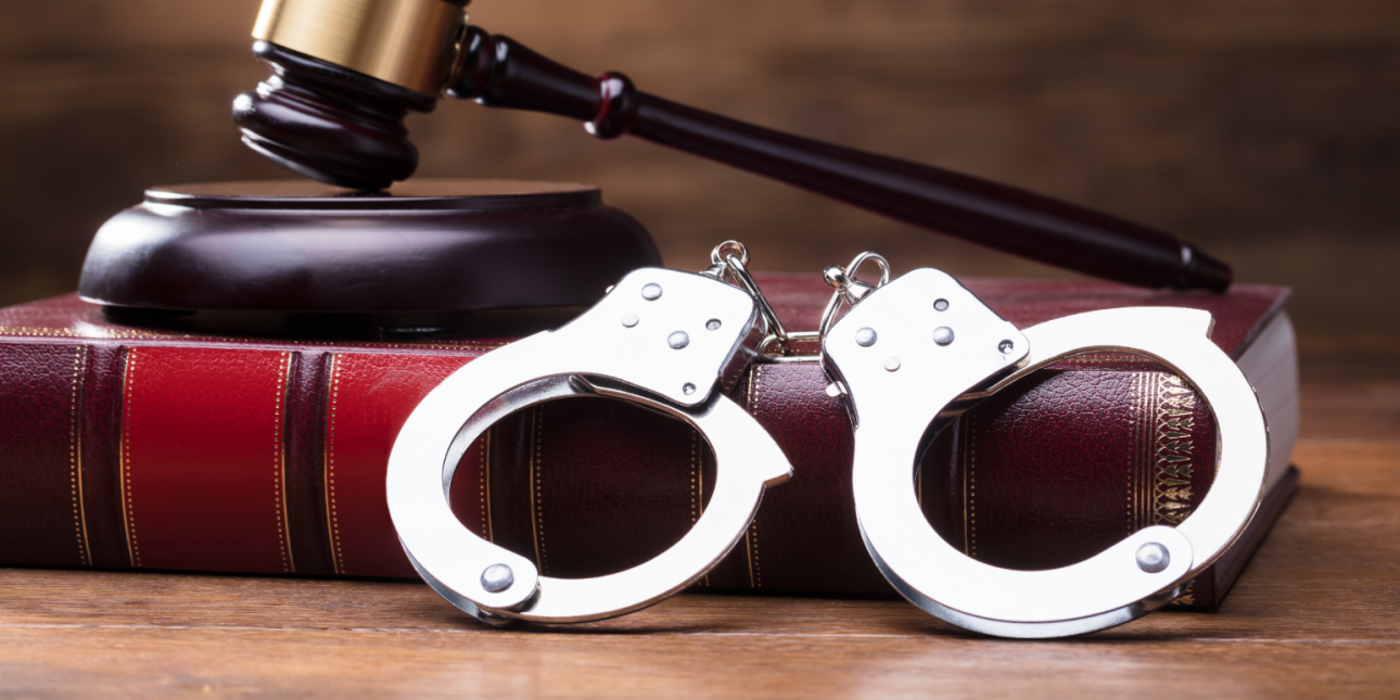 gavel sitting on top of a law book, with a pair of handcuffs in the foreground