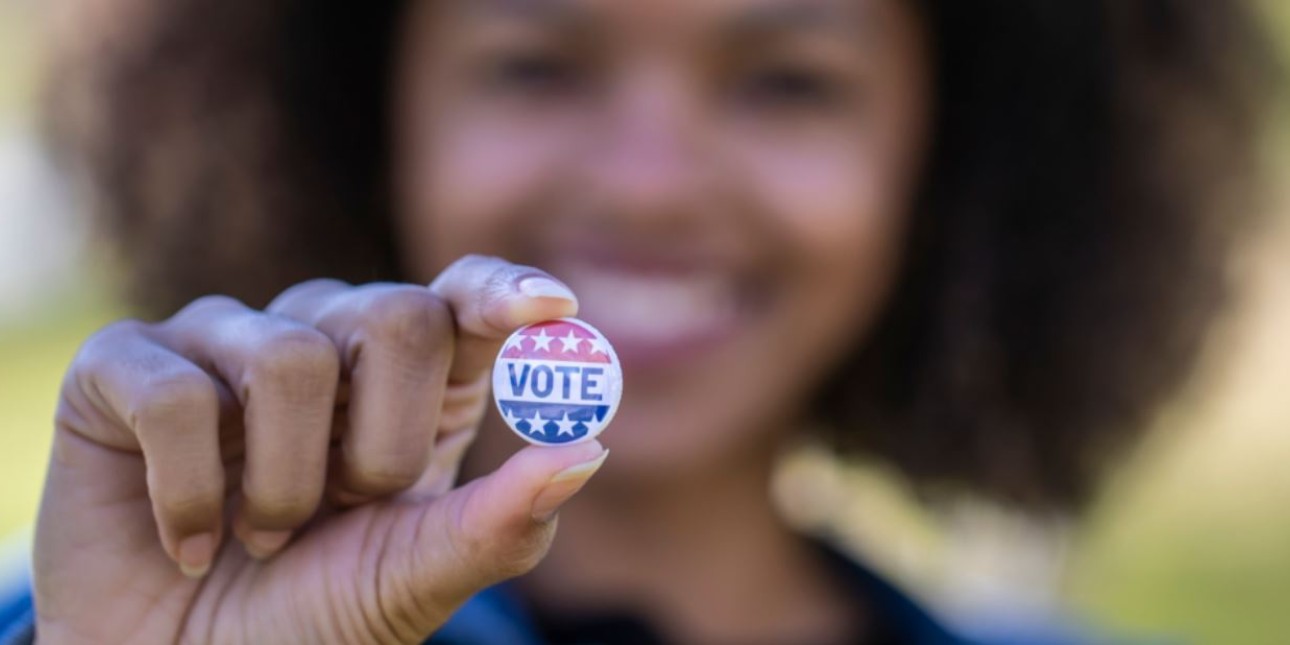 Woman holding up a red, white, and blue vote button
